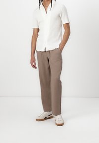 Biała teksturowana koszula z krótkim rękawem, beżowe luźne spodnie oraz kremowe sneakersy z czarnymi akcentami. Prosty design, casualowy krój i jasne kolory.