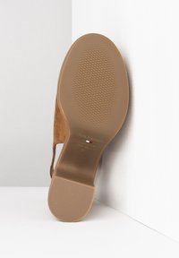 Semelle en daim marron avec une surface texturée en caoutchouc présentant une légère courbure et des détails de marquage imprimés en blanc.