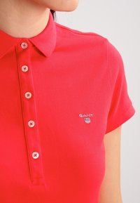 Camisa polo roja de manga corta, con un cuello clásico, tapeta de cinco botones y logo bordado en el lado izquierdo del pecho.