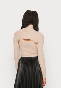Beige ribbed Strick-Turtleneck-Pullover mit offenen Rückenschlitzen, kombiniert mit einem schwarzen plissierten Rock, der texturale Kontraste zeigt.