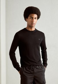 Black long-sleeve crew neck sweater made of soft material, features a small logo on the chest, paired with black drawstring shorts.