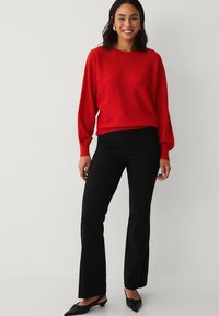 Rød strikket sweater med en afslappet pasform, ribbede manchetter, parret med sorte tætsiddende flared bukser og sorte slip-on sko. Enkle accessories.