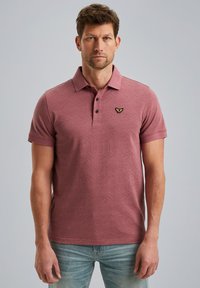 Polo-shirt à manches courtes de couleur rouge clair, avec un motif géométrique texturé, une patte de boutonnage à trois boutons et un petit emblème brodé sur la poitrine.
