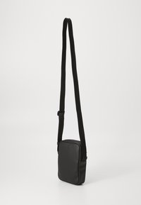 Geantă de umăr din piele neagră, cu un finisaj texturat, formă pătrată și curea din material ajustabilă. Design minimalist fără accesorii vizibile.
