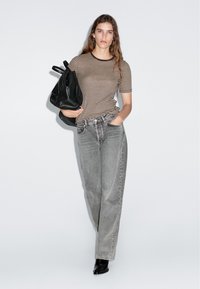 Pruhované hnědé a béžové tričko s kulatým výstřihem, spárované s šedými džíny s vysokým pasem. Černý batoh přes jedno rameno. Ploché černé kotníkové boty.