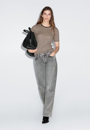 T-shirt a righe marrone e beige con scollatura rotonda, abbinato a jeans grigi a vita alta. Zaino nero su una spalla. Stivaletti neri flat.
