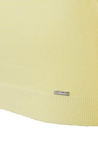 Gelber, gerippter Strickpullover mit strukturiertem Finish. Mit einem silbernen Etikett am unteren Rand, das den Markennamen zeigt.