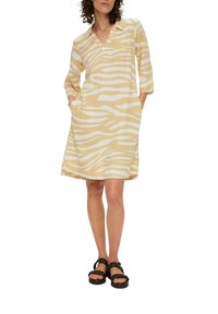 Beige Kleid mit weißen Zebrastreifen, Dreiviertelärmeln, einem V-Ausschnitt und Taschen; kombiniert mit schwarzen Plateausandalen.