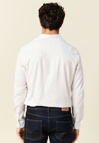 Weißes Hemd mit hellen vertikalen Streifen, langen Ärmeln und Kragen. Getragen mit dunkelblauen Jeans, die Rückendetails und Nähte zeigen.