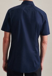 Marinblå kortärmad skjorta med spetsig krage, rak nederkant och slät tyg. Har en klassisk passform med rena linjer och inga synliga mönster.
