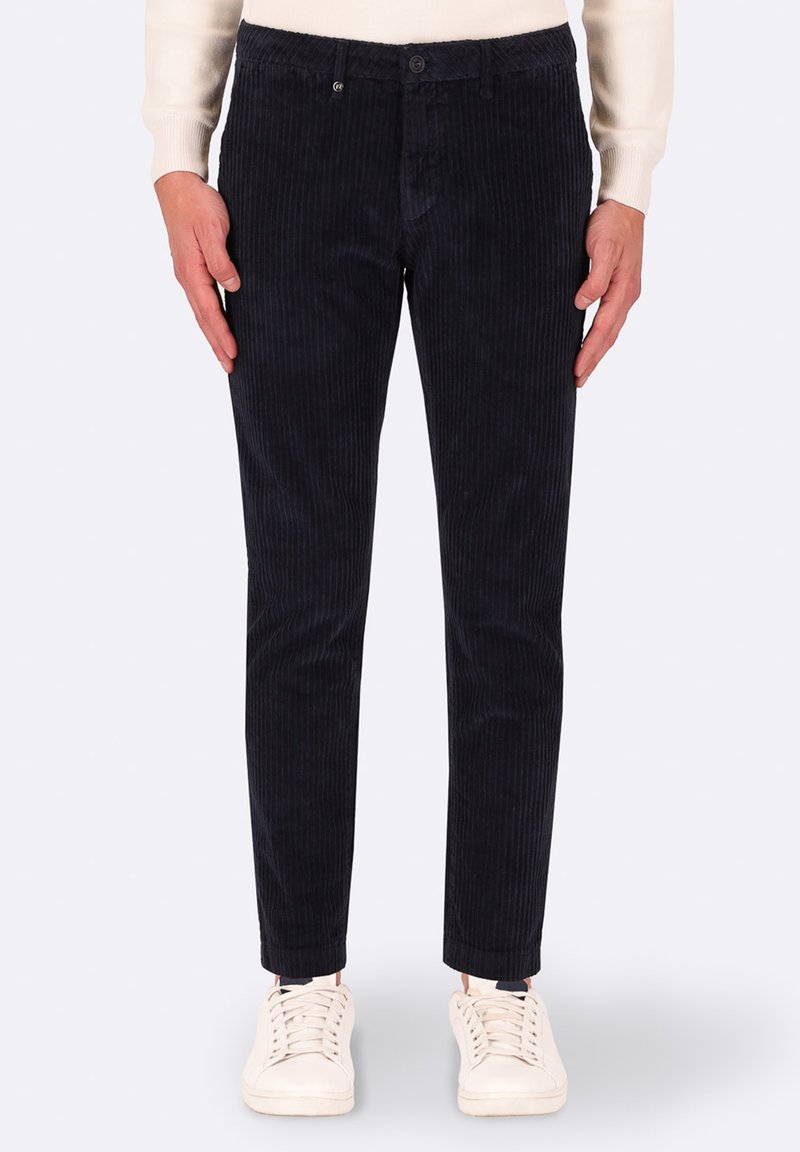 Pantaloni in velluto a coste blu navy con righe verticali, taglio slim, chiusura con bottone e una texture morbida, abbinati a sneaker bianche.