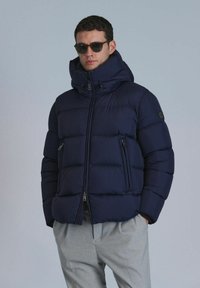 Navyblaue gepolsterte Daunenjacke mit hohem Kragen, durchgehendem Reißverschluss und zwei Seitentaschen. Glatte Textur, leicht und isoliert gestaltet.