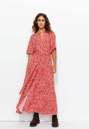 Robe maxi à motif paisley rouge avec un col et des manches courtes, dotée d'une taille à nouer et d'une silhouette fluide. Bottes chukka marron.