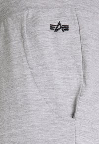 Un pantalon de survêtement gris en tissu doux et texturé avec un subtil motif chiné. Le design comprend une seule poche latérale et un logo brodé.