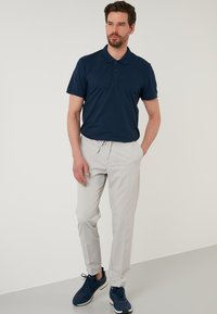 Námornická polo košile s texturovaným povrchem, spárovaná se světle šedými kalhotami a námořnickými teniskami. Tento outfit má uvolněný střih a krátké rukávy.