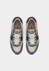 Ζευγάρι μπεζ και τυρκουάζ αθλητικά παπούτσια Converse με λευκά κορδόνια και μαύρο λογότυπο σε σχήμα βέλους, σε θέα από πάνω πάνω σε λευκό φόντο.