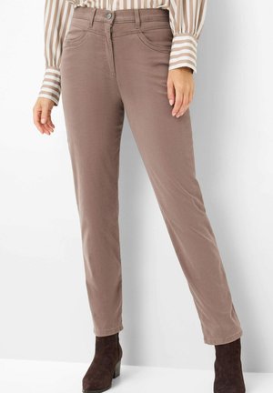 Woman wearing light brown slim-fit pants, striped long-sleeve blouse tucked in, and dark brown ankle boots standing against white background.