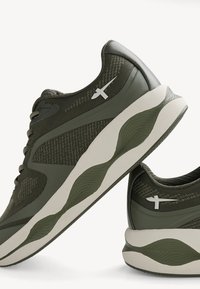Green athletic shoes feature a mesh upper with textured accents and a thick white sole. A reflective logo is on the side for visibility.