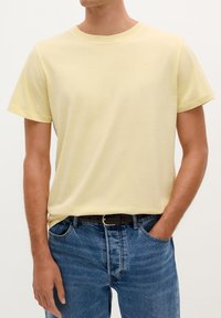Lichtgele katoenen t-shirt met een ronde halslijn en korte mouwen, gecombineerd met blauwe denim jeans en een zwarte riem.