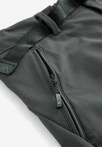 Gros plan sur un short en tissu gris foncé avec une poche zippée équipée d'un tirette de marque et une ceinture noire ajustable.