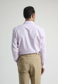 Camisa de manga larga rosa claro con puños abotonados; combinada con pantalones de lino beige que tienen bolsillos laterales y traseros. Textura lisa y uniforme.