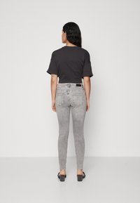 Grå, kortermet t-skjorte sammen med grå, tettsittende jeans. Jeansene har en jevn tekstur, minimal falming og klassiske baklommer. Svarte blokkhælsko.