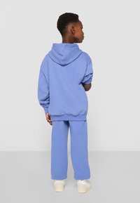 Felpa con cappuccio azzurro chiaro e pantaloni della tuta in tessuto morbido. Le maniche sono arrotolate e l'insieme ha una vestibilità rilassata.