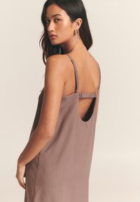 Ruda rankovių nesurišta suknelė su atvira nugara, plonomis petnešėlėmis ir surišimo detalėmis ant pečių. Lygi audinio tekstūra, paprastas dizainas.