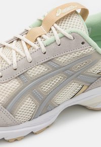 Ljusbrun nät-sneaker med grå och krämfärgade accenter, gummisula och subtila texturerade detaljer. Har en snörkrage i brunt och mintgrönt.