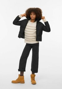 Sort puffjakke med glidelås og hette, beige stripete genser, mørke cropped jeans og gule ankelstøvler med lisser og gummisåler.