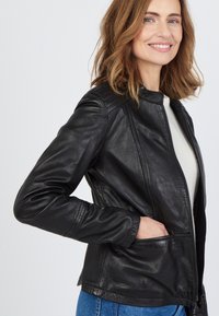 Svart skinnjacka med en figursydd design, hög krage och subtila sömnadsdetaljer. Har dragkedjestängning och sidofickor.