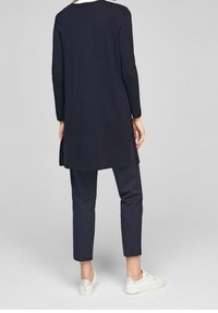 Marinblå långärmad tunika med rak skärning, rundad halsringning och sidofickor, i kombination med marinblå tapered-byxor och vita sneakers.