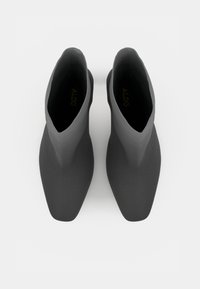 Stivali neri alla caviglia con una finitura liscia e opaca, punta appuntita e un design elegante e minimalista. Presentano un marchio interno impresso in oro.