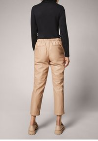 Pantalon en similicuir beige à coupe décontractée, taille élastique et deux poches arrière, associé à un haut noir à manches longues.