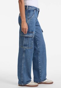 Denim-Cargohosen in mittlerem Blau mit bequemer Passform. Mit Seitentaschen, kontrastierenden Nähten und umgeschlagenen Säumen.