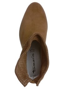 Stivaletto color tan in materiale scamosciato liscio, con perforazioni circolari attorno alla caviglia e punta arrotondata. Logo visibile all'interno della scarpa.