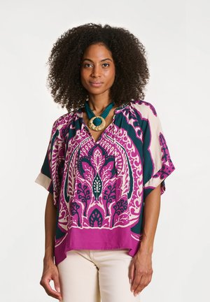 Blouse en coton colorée présentant un motif floral audacieux en magenta et sarcelle, avec un col en V, des manches courtes et une coupe décontractée.