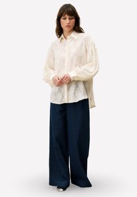 Licht gestructureerd, roomkleurig overhemd met een knoopsluiting aan de voorkant en omslagmouwen, gecombineerd met wijduitlopende marineblauwe ribgebreide broek.