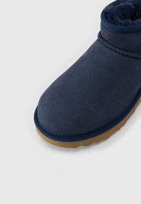 Χειμερινή μπλε ναυτική μπότε με λεπτομέρειες ραφής, μαλακή εσωτερική επένδυση και καφέ λαστιχένια σόλα σε φωτεινό φόντο.