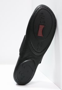Suela de zapato de cuero negro con superficie texturizada y bordes redondeados. Presenta la marca "Camper" en rojo en la parte inferior y detalles decorativos.