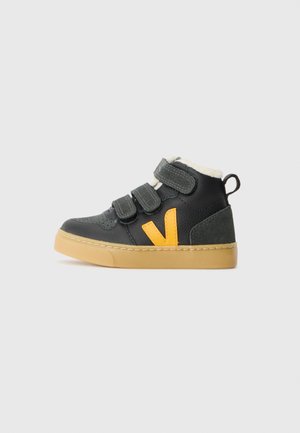 Baskets montantes noires pour enfant avec trois straps velcro, semelle beige, logo jaune sur le côté et doublure en polaire blanche à l'intérieur.