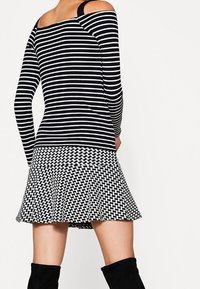 Sort-hvide stribede langærmede toppe overgår til en flagrende, vævet mønstret nederdel, som har en afslappet pasform og off-shoulder design.