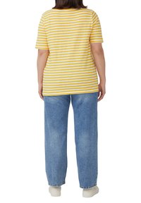 Gelb-weiß gestreiftes T-Shirt mit kurzen Ärmeln, kombiniert mit hellblauen weiten Jeans und weißen Turnschuhen. Rückansicht.