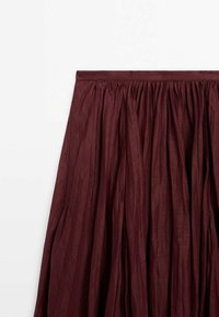 Jupe plissée bordeaux avec une taille froncée, tissu fluide, et motif texturé sur fond blanc uni.