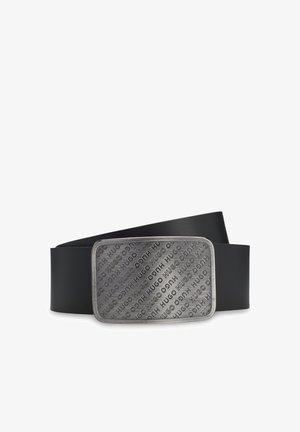 Ceinture en cuir noir avec une grande boucle rectangulaire argentée embossée à plusieurs reprises du nom de la marque « HUGO » dans différentes orientations.