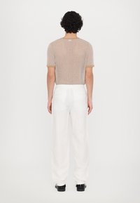Chemise beige à manches courtes en tricot avec un motif texturé, associée à un pantalon en lin blanc ample et des chaussures noires, vue de dos.