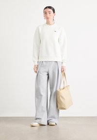 Felpa bianca, pantaloni larghi grigi e borsa a tracolla beige. Tessuto morbido, design semplice, con un logo discreto sulla felpa.