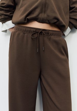 Smeđe trenirke s elastičnim pojasom i bočnim džepovima, izrađene od mekanog, teksturiranog materijala. Imaju opušteni kroj i suptilne detalje šavova.