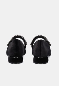 Zapatos de ante negro con un tacón bajo, que presentan una punta redonda y una correa de cuentas en la parte trasera. Textura suave con una suela pulida.