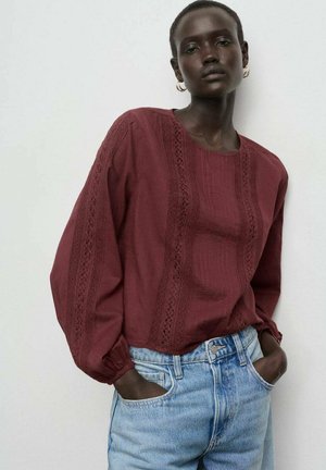 Blusa burdeos de manga larga con rayas verticales texturizadas y acentos de encaje, combinada con vaqueros de mezclilla de lavado claro. Tejido suave y corte relajado.